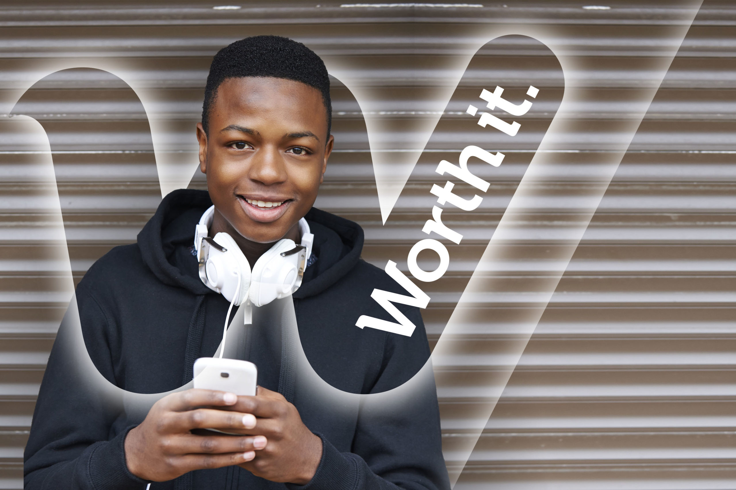 A young man holding a cell phone in front of a wall.