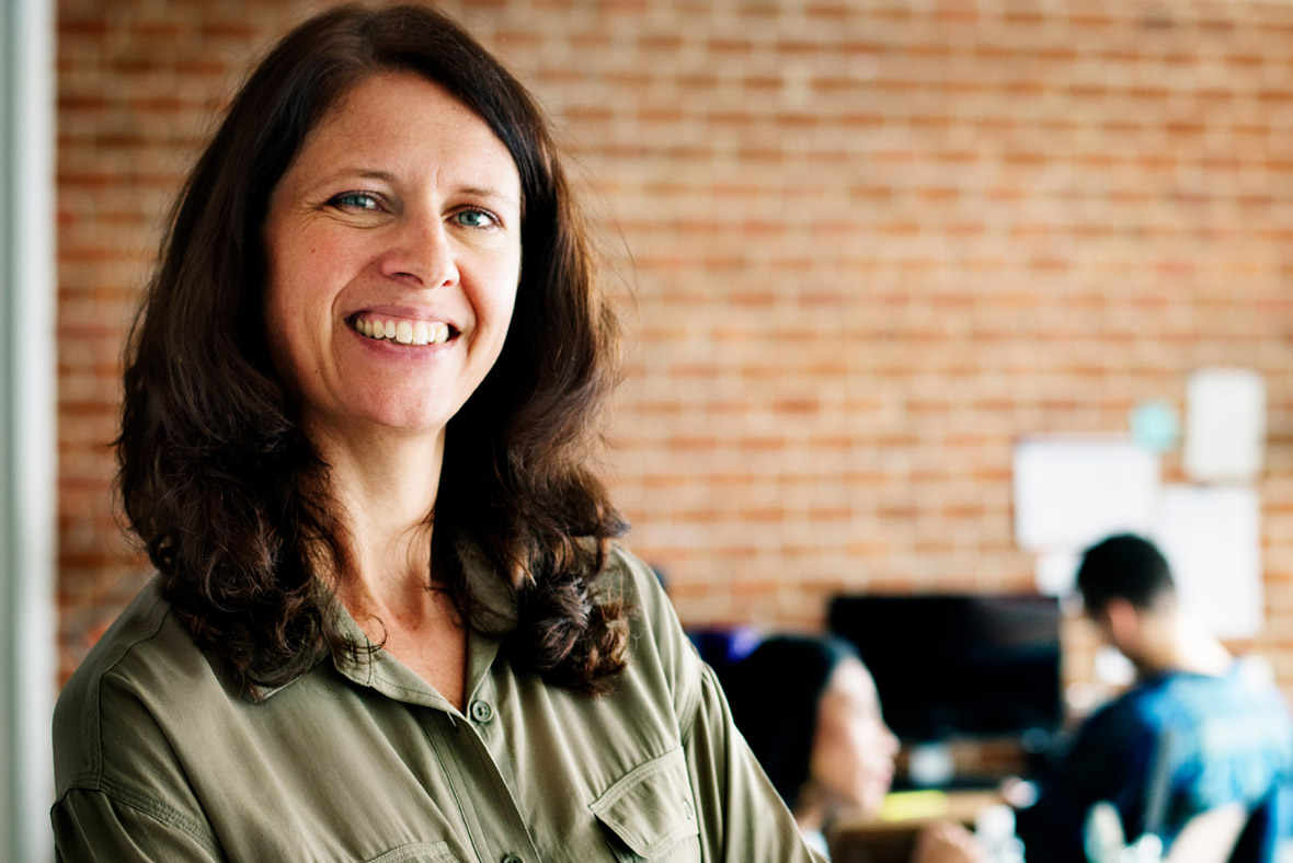 A woman smiling in front of a brick wall.