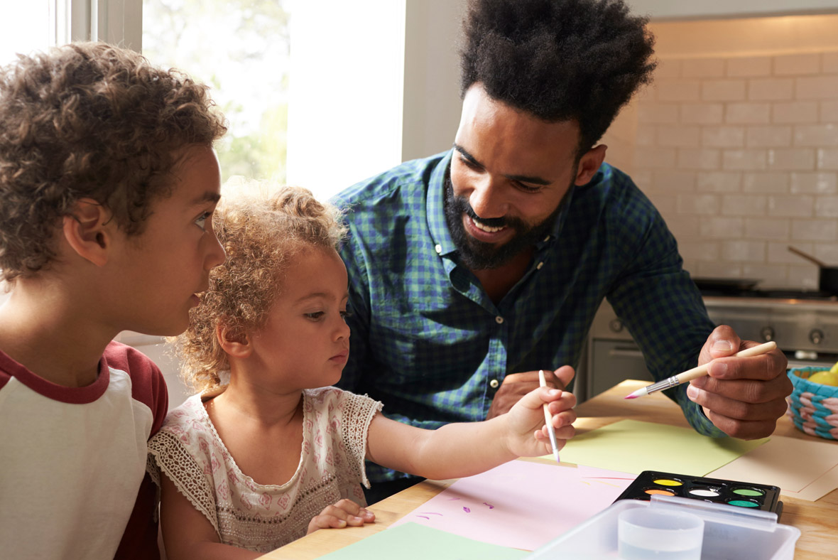 A man and two children are painting together at a table.