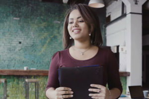 A woman stood in a room holding a black folder