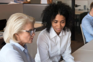 A young woman helping an older colleage at a desk