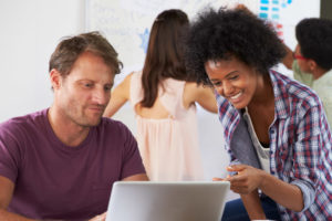 A woman talking to a male colleague at a computer