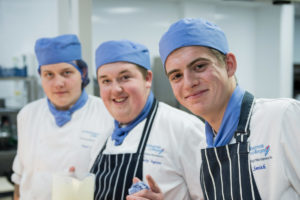 A photo of three people in a professional kitchen looking positive