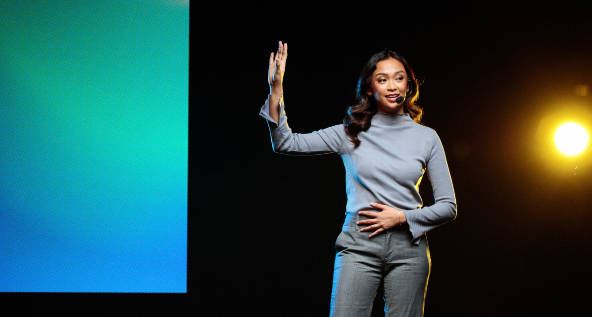 A woman is standing in front of a large screen, preparing for a public speaking engagement.